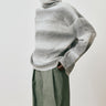 Person wearing a large, loose-fitting gray sweater with green pants against a plain background