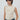 a beige ruched sleeveless top and blue jeans, standing against a light gray studio background.