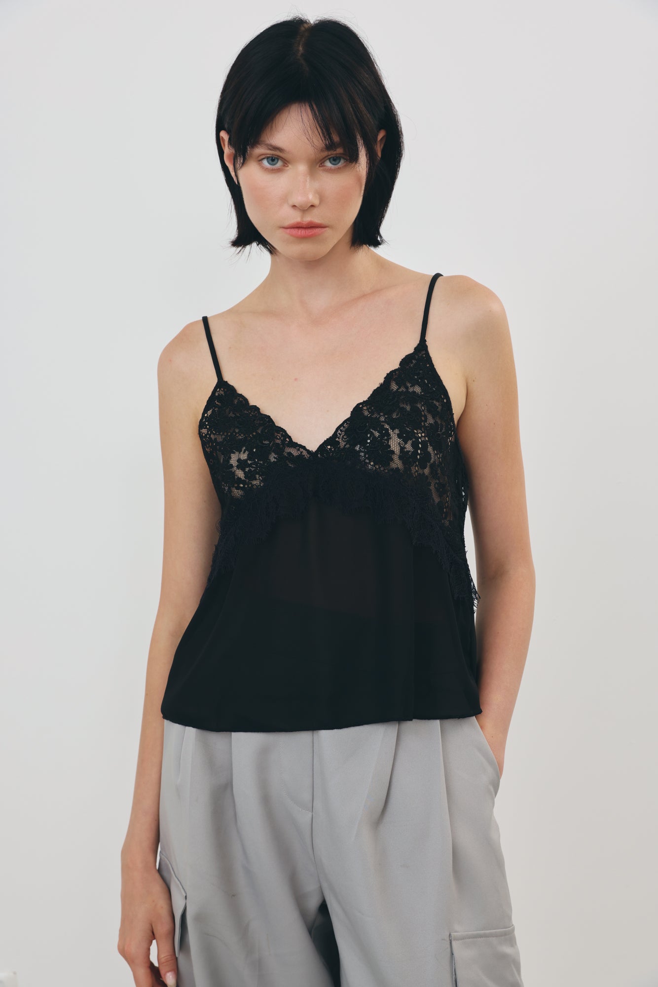 A model wearing a black lace camisole top with thin straps and light manta cargo pants