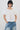 A model wearing a white short-sleeve blouse with voluminous puff sleeves and a smocked neckline, paired with light-wash blue jeans, against a plain light gray background.