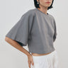 a gray cropped t-shirt with wide, voluminous sleeves and white pants, styled with black sunglasses against a plain light gray background.