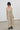 A model wearing a saga smocked midi dress with thin spaghetti straps, styled with black sunglasses, gold hoop earrings, and black leather loafers, standing against a minimalist white wall and gray floor.