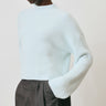 Person wearing a light blue sweater and dark gray pants against a plain background