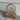 A beige vegan suede bowler bag with a classic silhouette, displayed against a textured background.